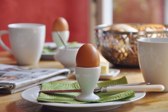 Das Foto zeigt einen gedeckten Frühstückstisch mit einem Ei im Eierbecher