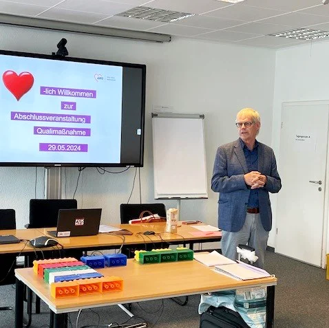 Das Foto zeigt Jürgen Otto in dem Seminarraum. Im Hintergrund ist ein Whiteboard mit dem Text "Herzlich Willkommen zur Abschlussveranstaltung Qualimaßnahme 29.05.2024"