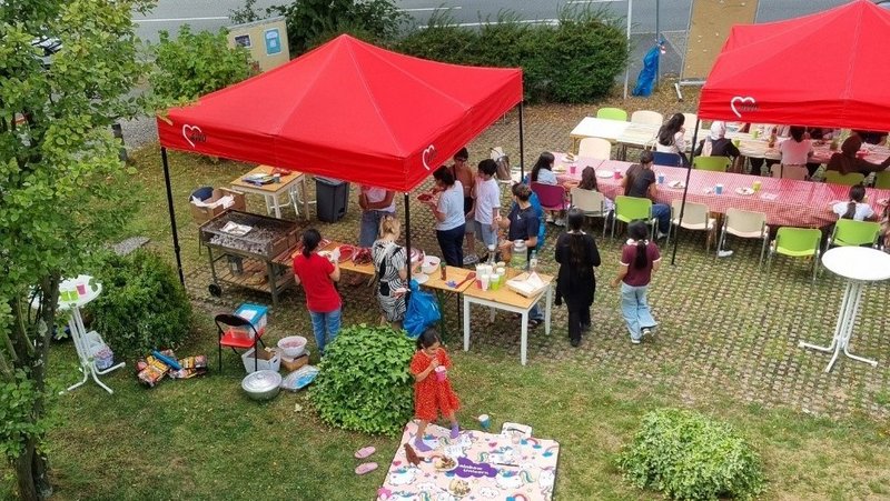 Sommerfest unter roten Pavillons – Familien und Freunde genießen gemeinsam einen sonnigen Tag mit Spielen, Gesprächen und Picknick im Grünen