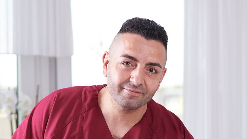 Das Foto zeigt ein Portrait von Arslan Aziz. Er trägt rote Dienstkleidung und befindet sich in einem Zimmer der Einrichtung