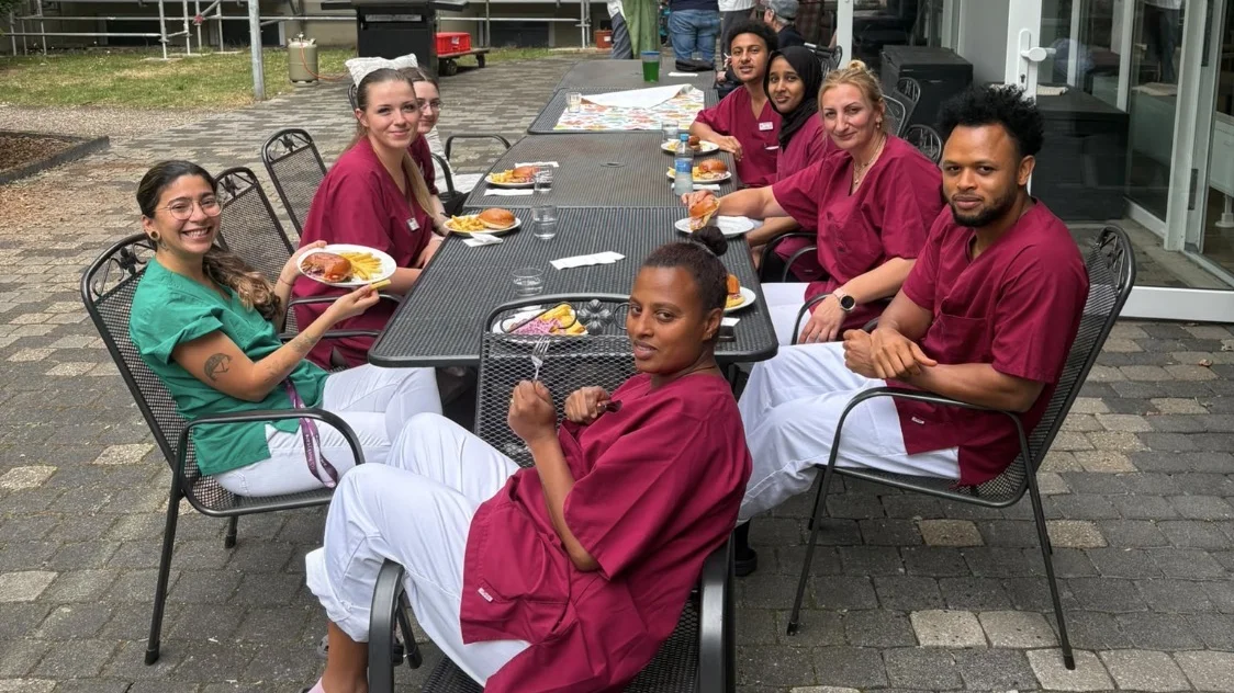 Auf diesem Bild sind Mitarbeitende zu sehen, wie sie ihren Burger im Innenhof der Einrichtung genießen.