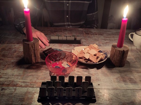 Das Bild zeigt zwei Kerzen die brennen, während eine Familie ein Gesellschaftsspiel spielt