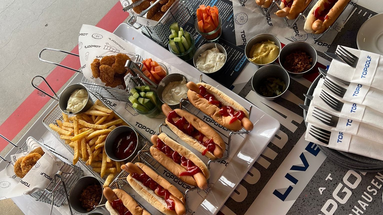 Dieses Bild zeigt Hotdogs, Nuggets und Pommes auf dem Tisch bei Topgolf Oberhausen.