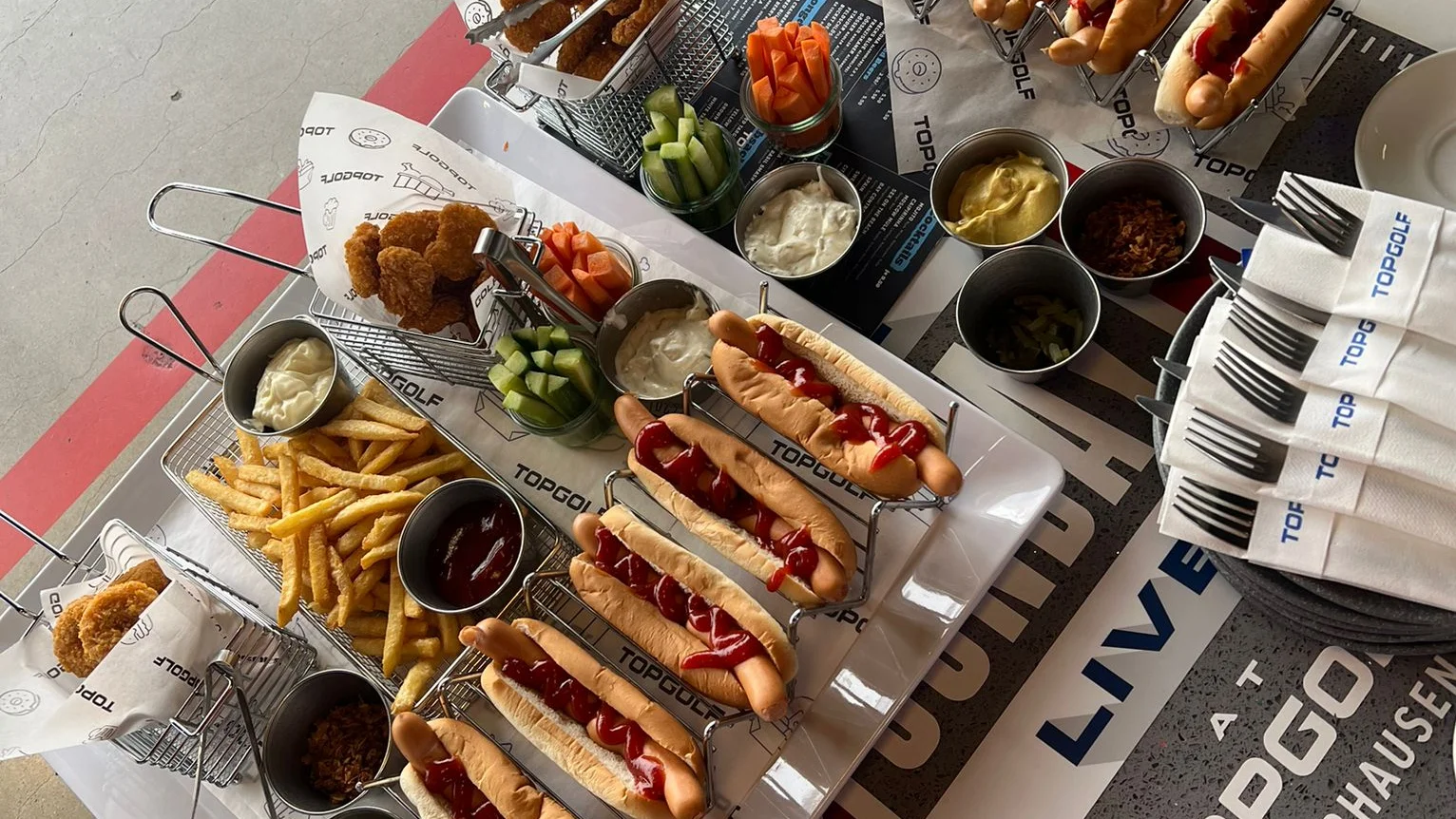 Dieses Bild zeigt Hotdogs, Nuggets und Pommes auf dem Tisch bei Topgolf Oberhausen.