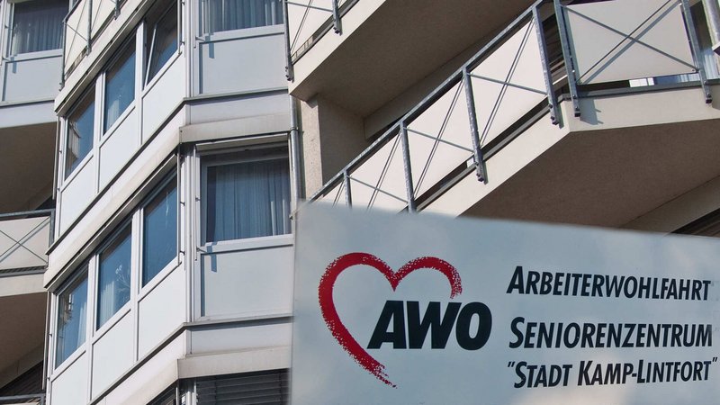 Auf dem Foto ist ein Gebäude zu sehen, bei dem es sich offenbar um ein Seniorenheim handelt. Im Vordergrund befindet sich ein Schild mit der Aufschrift: „AWO Arbeiterwohlfahrt Seniorenzentrum ‚Stadt Kamp-Lintfort‘“ Das Schild zeigt auch das bekannte AWO-Logo, bestehend aus einem stilisierten roten Herz und dem Schriftzug „AWO“.