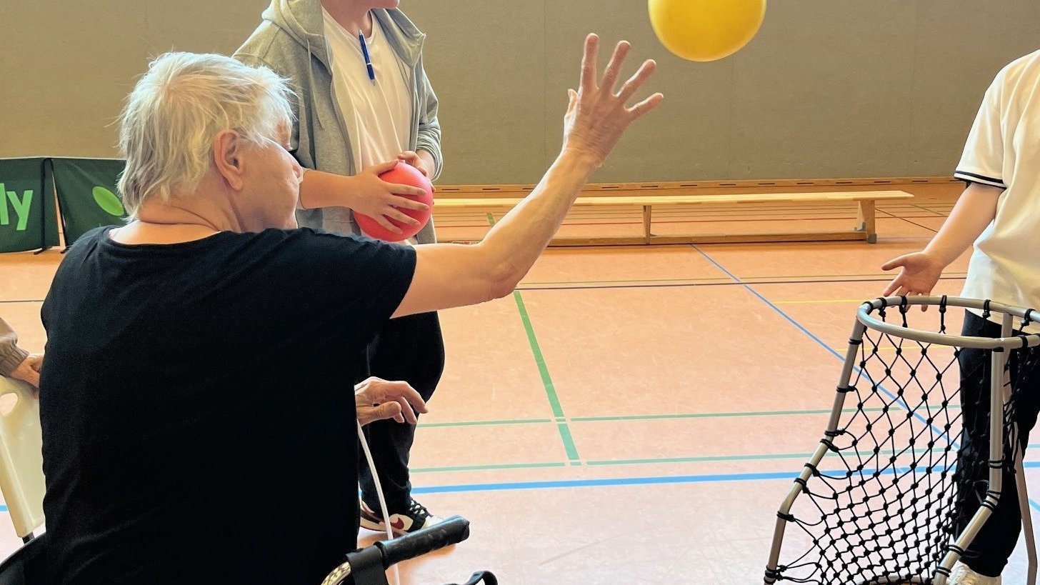 Auf dem Bild sieht man eine ältere Frau im Rollstuhl bei einem Wurf auf einen Basketballkorb.