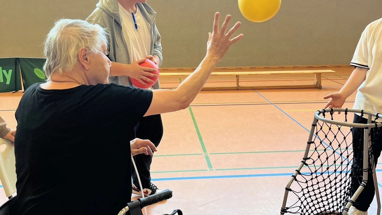 Auf dem Bild sieht man eine ältere Frau im Rollstuhl bei einem Wurf auf einen Basketballkorb.