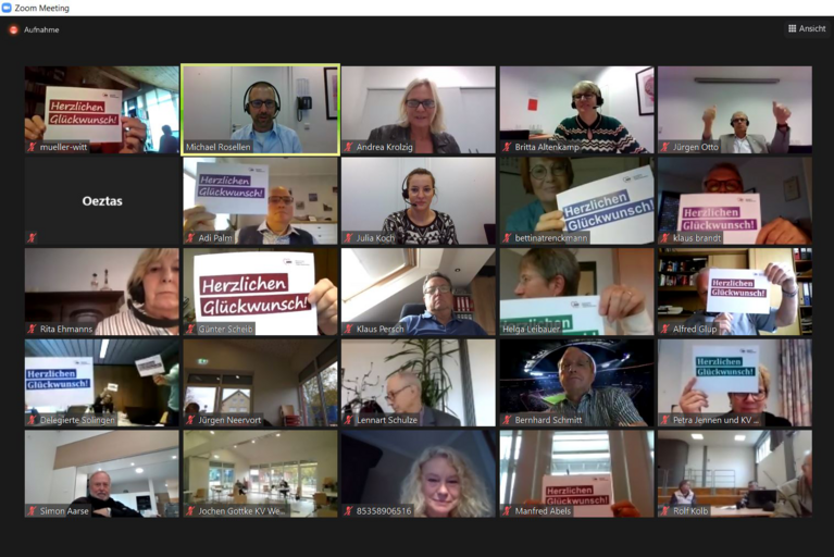 Screenshot aus der Videokonferenz mit Delegierten, die eine Gratulationskarte in der Hand haben