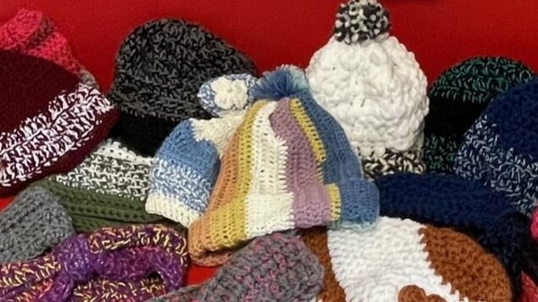 Auf dem Bild ist eine bunte Sammlung von handgearbeiteten Kopfbedeckungen und Accessoires zu sehen, die auf einer roten Fläche (vermutlich ein Sofa oder eine Bank) ausgebreitet sind. Hier sind die Details im Überblick: Mützen: Es gibt eine Vielzahl an gehäkelten oder gestrickten Mützen in unterschiedlichen Stilen, Farben und Mustern. Einige haben Bommel, andere sind schlicht gehalten oder mit kleinen Häkelblumen verziert. Stirnbänder: Im Vordergrund liegt ein graues, gehäkeltes Stirnband mit einer kleinen rosa Blüte sowie ein lilafarbenes Stirnband. Materialien: Die Gegenstände scheinen aus dicker Wolle gefertigt zu sein, was auf warme Winterkleidung hindeutet. Kontext: Der Dateiname „Drogenhilfe_Mutzenspende“ lässt darauf schließen, dass es sich um Spenden für eine soziale Einrichtung handelt, die an bedürftige Menschen verteilt werden.