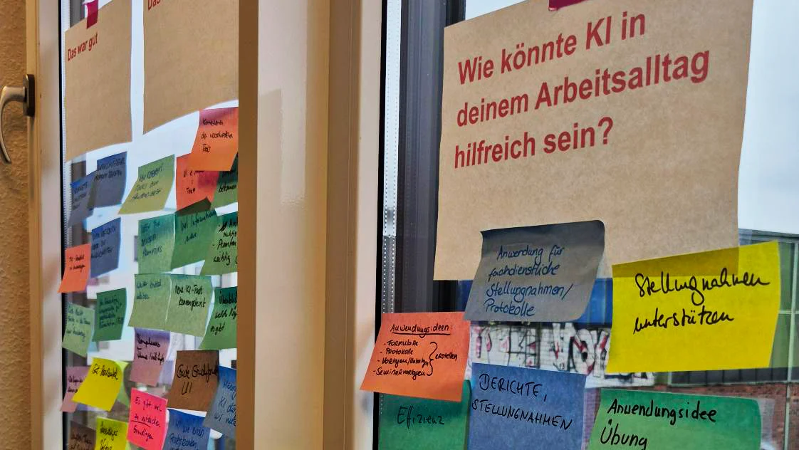 Auf dem Bild ist eine Fensterfläche oder eine Glastür zu sehen, auf der eine Sammlung von Post-it-Notizen (Klebezetteln) angebracht ist. Es sieht nach dem Ergebnis eines Workshops oder eines Brainstormings aus, da die Notizen in verschiedenen Farben und mit handschriftlichen Texten versehen sind.