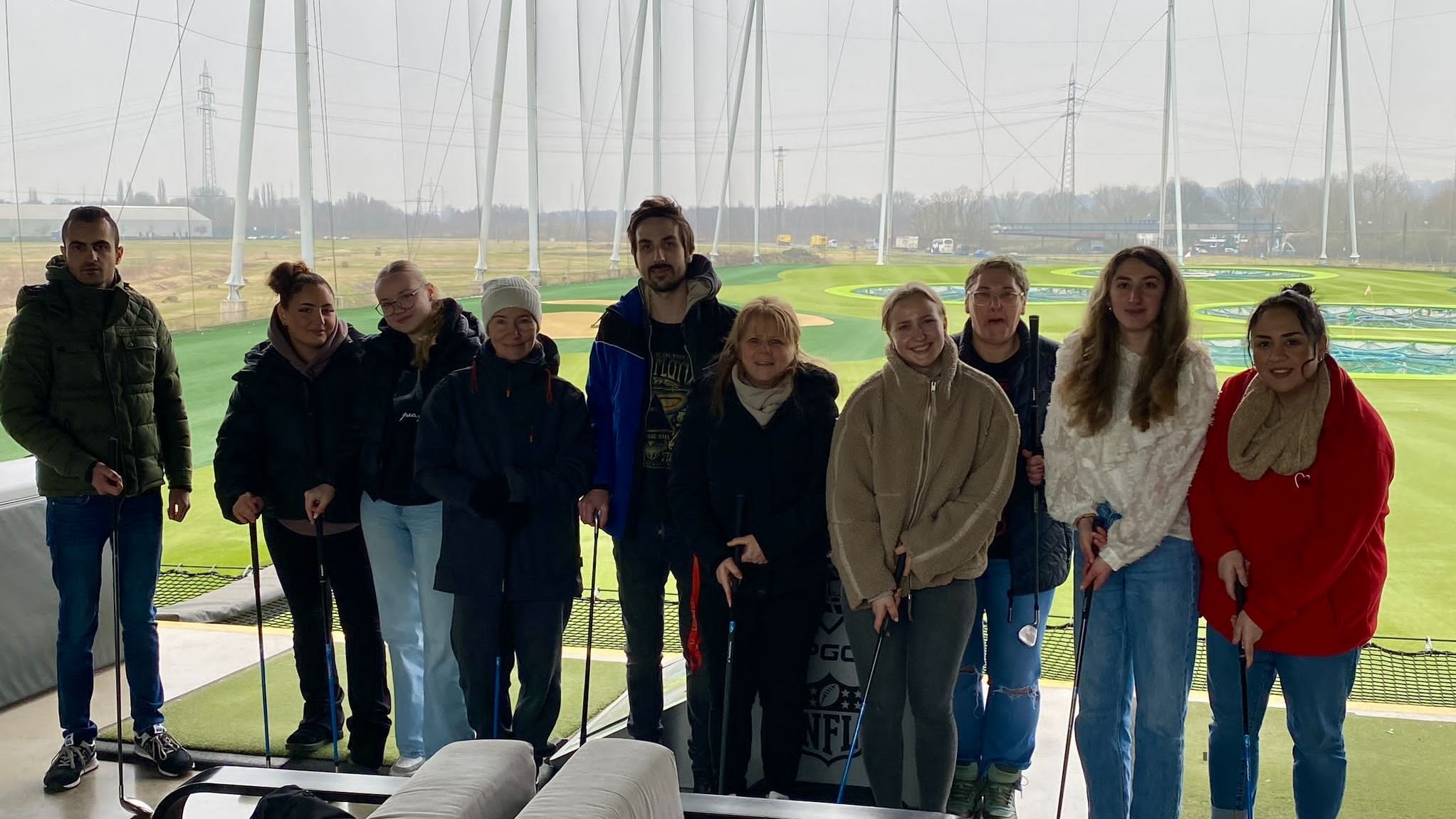 Dieses Bild zeigt das Gruppenfoto der Azubis vor dem Abschlagbereich bei Topgolf Oberhausen.