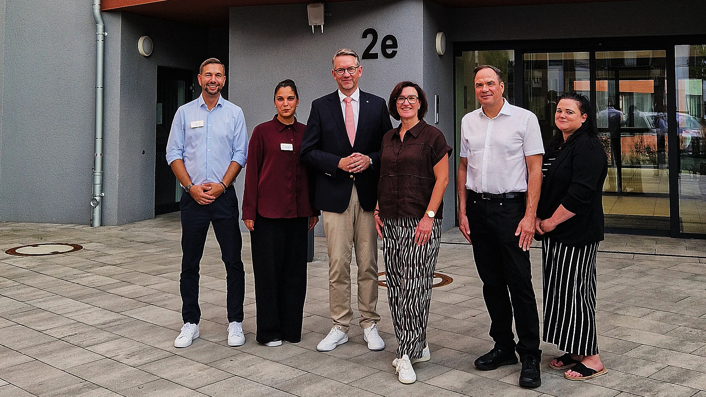 Auf dem Foto ist eine Gruppe von sechs Personen vor dem AWO-Seniorenzentrum „Am Wasserschloss“ zu sehen. Das Gebäude trägt ein auffälliges rotes AWO-Logo sowie den Schriftzug „Am Wasserschloss“. Die Personen stehen vor dem Eingangsbereich, der mit „2e“ gekennzeichnet ist.