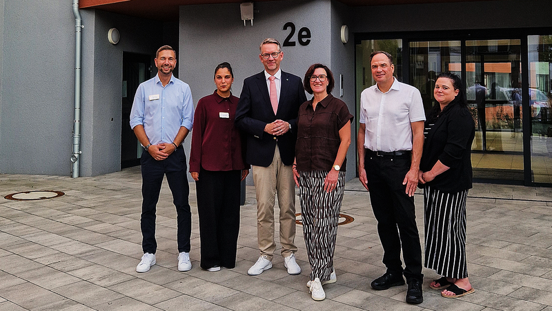 Auf dem Foto ist eine Gruppe von sechs Personen vor dem AWO-Seniorenzentrum „Am Wasserschloss“ zu sehen. Das Gebäude trägt ein auffälliges rotes AWO-Logo sowie den Schriftzug „Am Wasserschloss“. Die Personen stehen vor dem Eingangsbereich, der mit „2e“ gekennzeichnet ist.