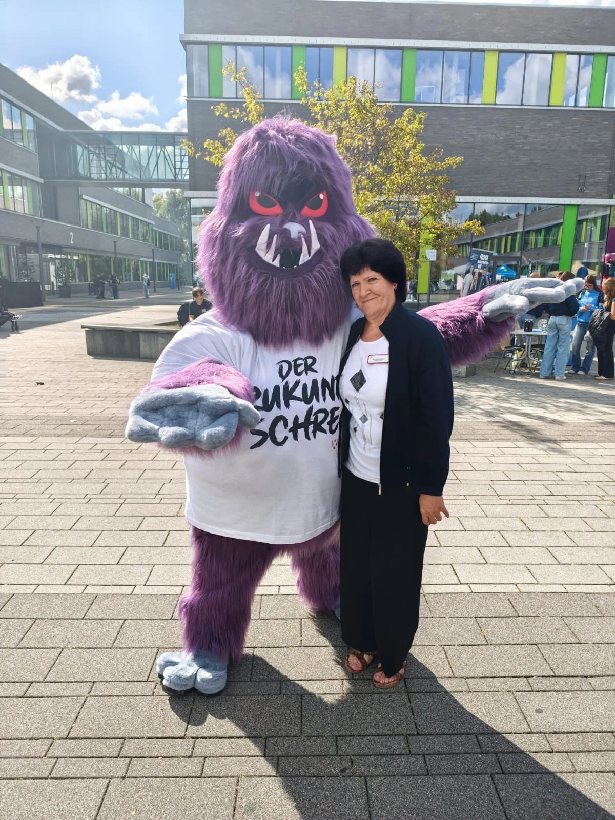 Das Bild zeigt eine Mitarbeiterin neben einem weiteren Maskottchen der Messe.