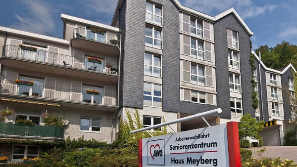 Auf dem Bild ist ein mehrstöckiges Gebäude mit Balkonen zu sehen, offenbar ein Wohn- oder Seniorenzentrum. Im Vordergrund steht ein Schild mit der Aufschrift „Arbeiterwohlfahrt Seniorenzentrum Haus Meyberg“.