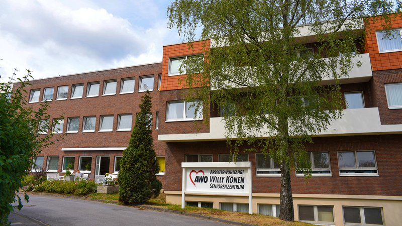 Zu sehen ist ein mehrstöckiges Gebäude mit dem Schild „AWO Willy Könen Seniorenzentrum“ am Eingang. Es handelt sich offenbar um eine stationäre Pflege- oder Senioreneinrichtung der Arbeiterwohlfahrt (AWO); vor dem Haus stehen Bäume und Sträucher.