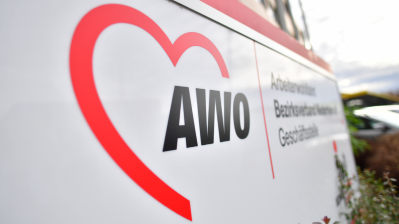 Auf dem Bild ist ein Schild des AWO Bezirksverbands Niederrhein zu sehen. Es zeigt das rote AWO-Herzlogo sowie den Schriftzug „AWO“; daneben steht „Arbeiterwohlfahrt Bezirksverband Niederrhein“.