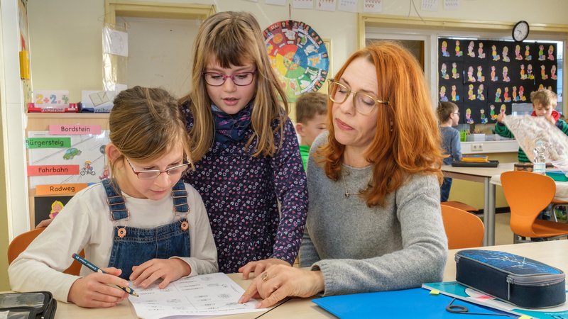 Das Foto zeigt eine Frau mit zwei Kindern in einem Klassenzimmer