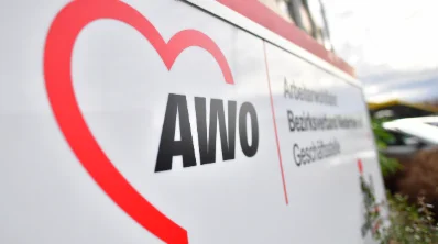 Das Schild zeigt das Logo der Arbeiterwohlfahrt (AWO) mit einem roten Herzsymbol und dem Schriftzug „AWO“ in schwarzer Schrift