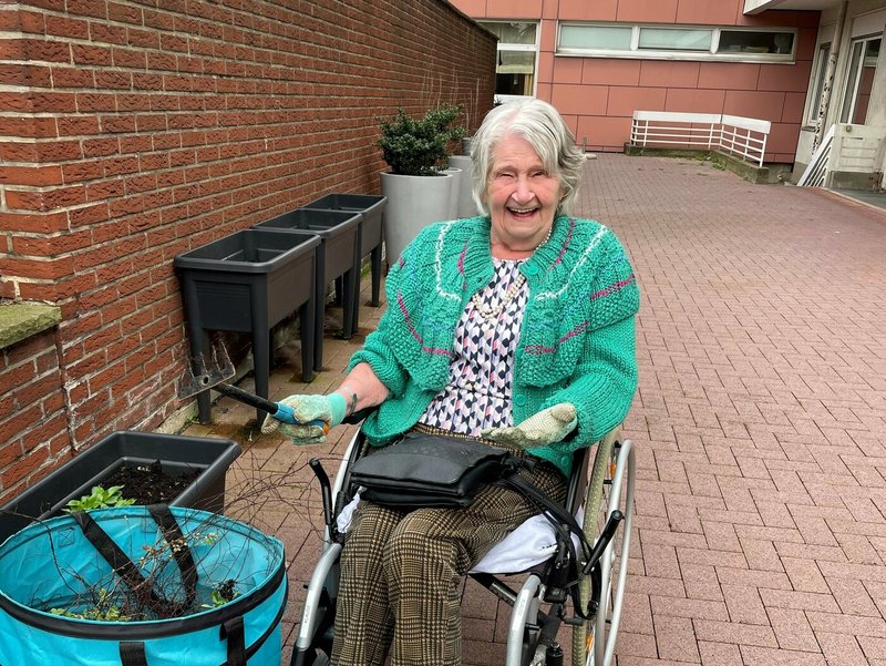 Das Foto zeigt eine Bewohnerin im Rollstuhl die den Innenhof des Seniorenzentrums Karl-Jarres-Straße von Unkraut befreit