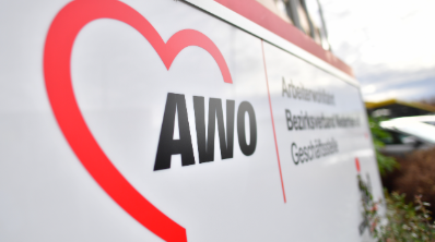Das Schild zeigt das Logo der Arbeiterwohlfahrt (AWO) mit einem roten Herzsymbol und dem Schriftzug „AWO“ in schwarzer Schrift