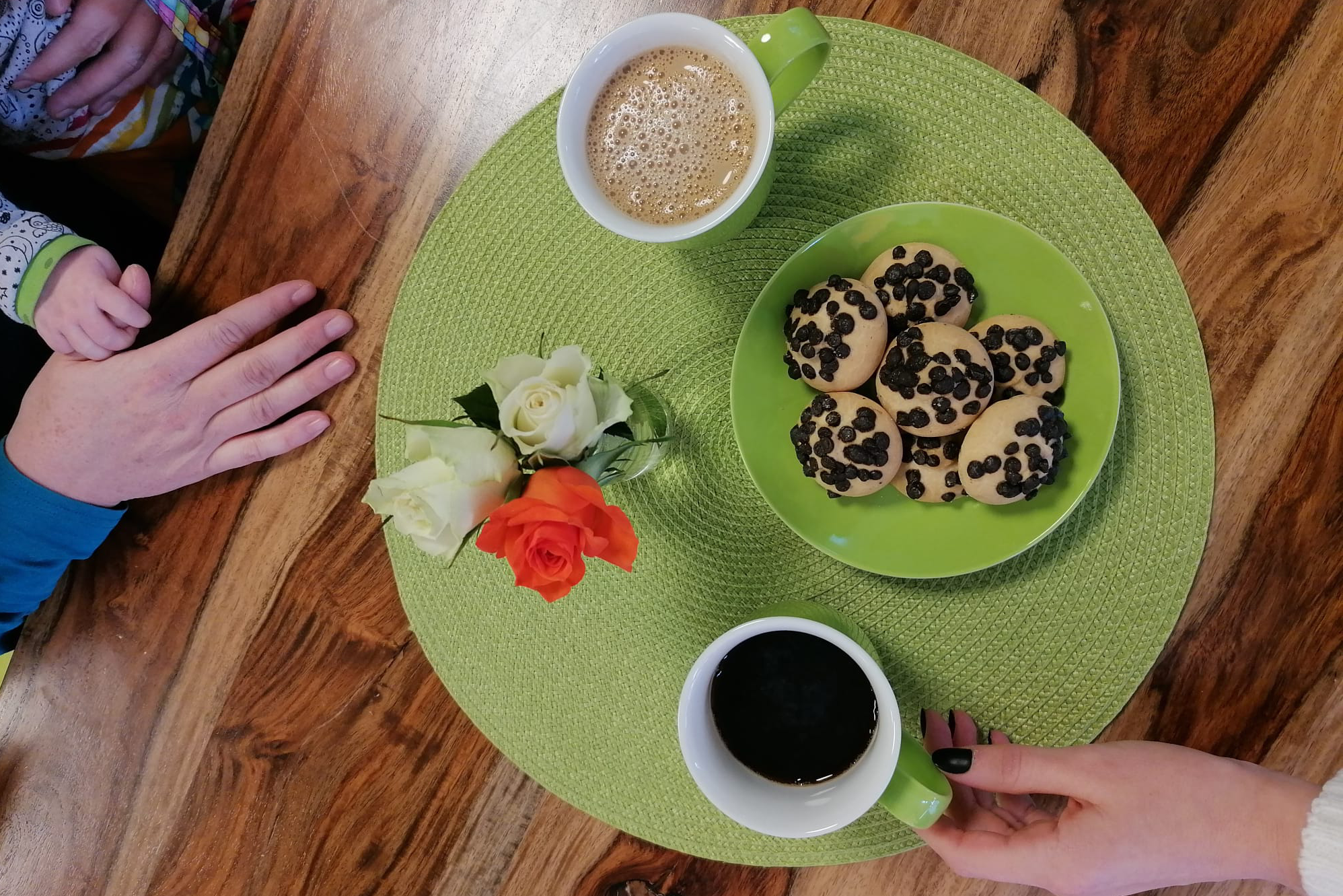 Das Bild zeigt eine Kinderhand, die auf einer Erwachsenenhand liegt und einen Frühstückstisch