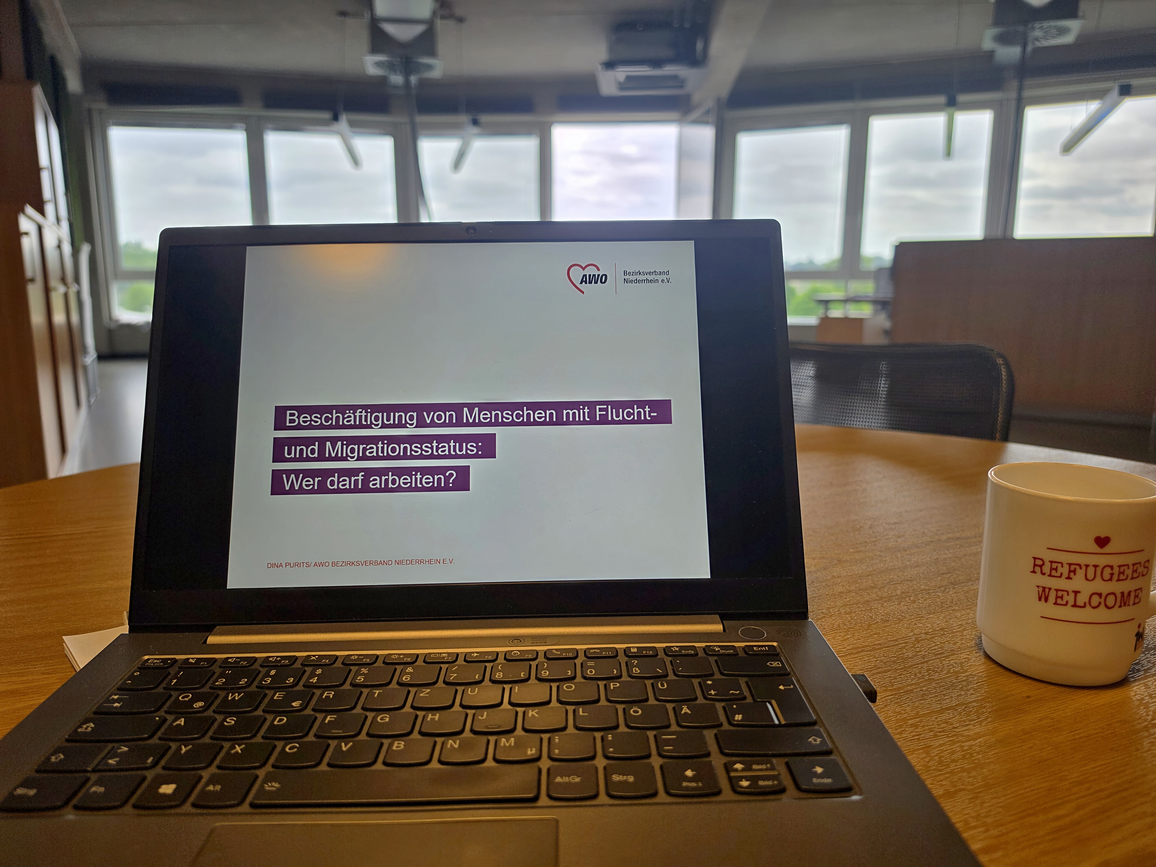 Arbeitsplatz mit Laptop-Präsentation zum Thema Arbeitsmarktzugang für Menschen mit Flucht- und Migrationsgeschichte in einem Seminarraum.