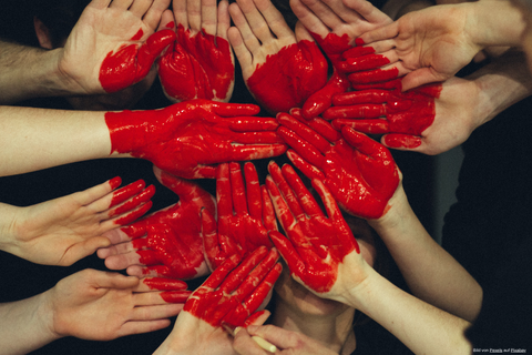 Das Foto zeigt viele rot angemalte Hände, die ein Herz bilden