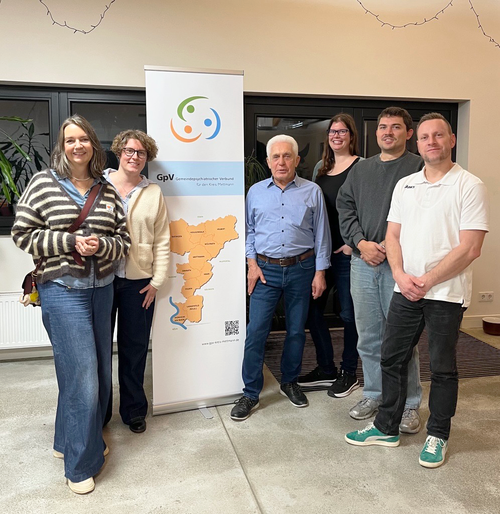 Auf dem Foto sind sechs Personen zu sehen – drei Frauen und drei Männer – die vor einem aufgestellten Banner stehen. Das Banner hat ein Logo und den Text "GPV Gemeindepsychiatrischer Verbund für den Kreis Mettmann" und zeigt eine Karte des Kreises Mettmann mit eingezeichneten Städten. Die Personen stehen im Innenbereich.