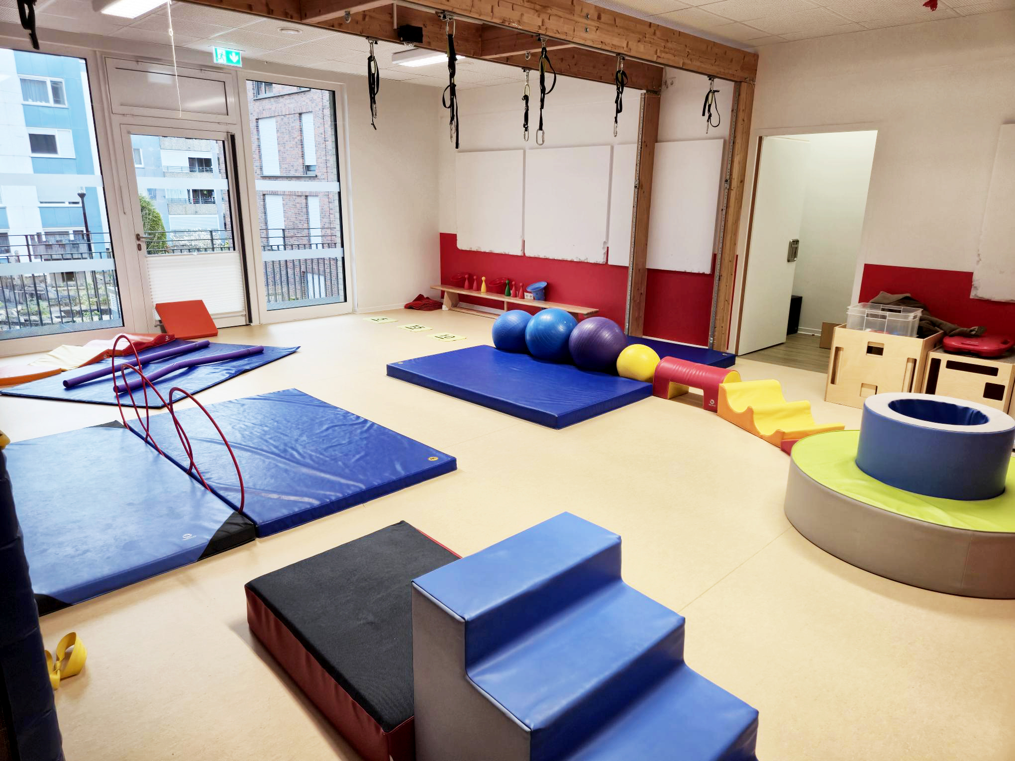 Auf dem Bild ist ein heller Bewegungsraum in der Kita zu sehen, in dem verschiedene Turn- und Spielmaterialien wie Matten, Bälle, Kletter- und Rutschelemente sowie eine Bewegungsbaustelle aufgebaut sind.